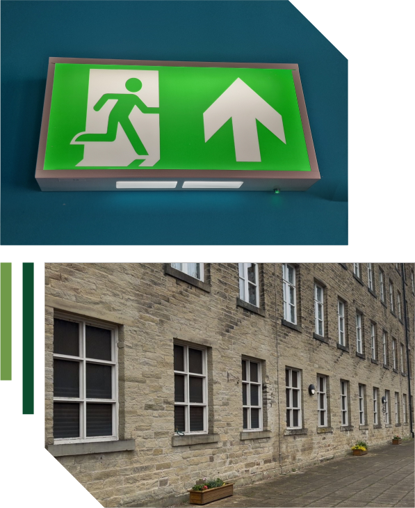 A green emergency exit sign with a running figure and upward arrow, often maintained by landlords or electrical services, above a photo of a stone building with several windows and a paved footpath. | Green View Projects